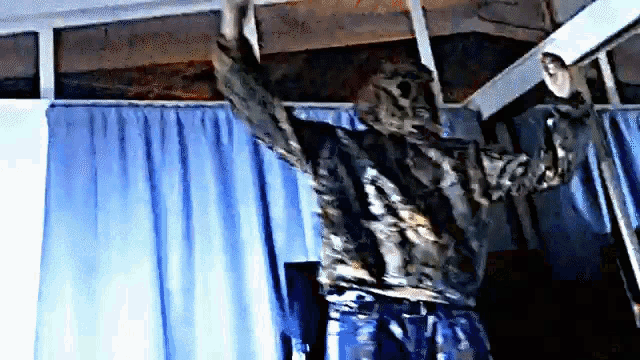 a person is standing on a ladder with their arms outstretched in a room with blue curtains .