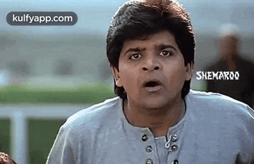 a man in a gray shirt is making a funny face with his mouth open .