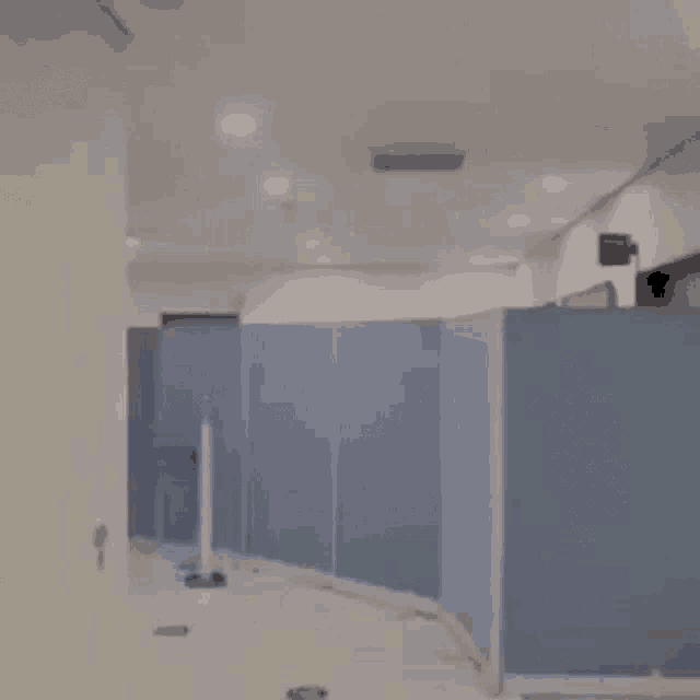 a person is walking down a hallway with blue dividers and a door .