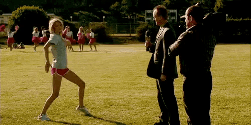 a woman is dancing in a field while a man in a suit stands behind her .