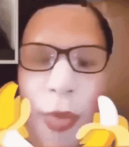 a man wearing glasses is eating a banana with his tongue out .