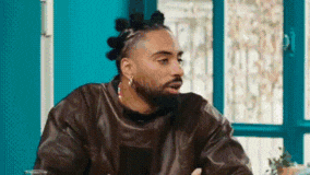 a man with dreadlocks and a beard is sitting at a table with his hands folded .