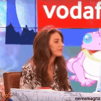 a woman sits at a desk in front of a sign that says vodafone