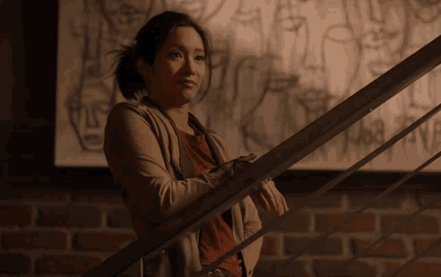 a woman leans on a railing in front of a wall with a drawing of a woman