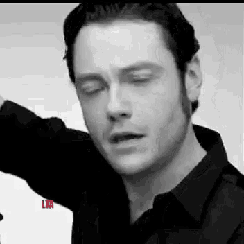 a black and white photo of a man in a black shirt with his eyes closed and his arm outstretched .