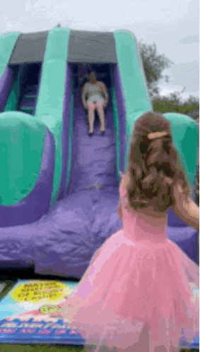 a little girl in a pink dress is standing next to a bouncy house .