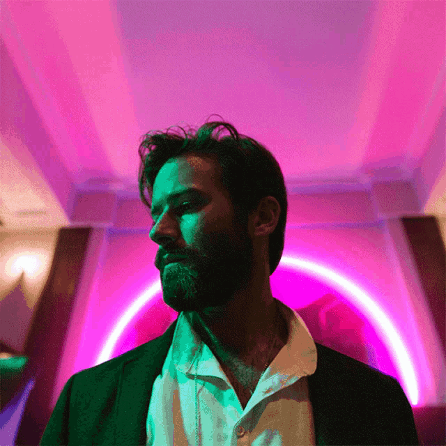 a man with a beard is standing in front of a purple and green light