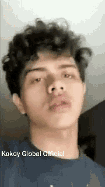 a young man with curly hair is taking a selfie with his mouth open .