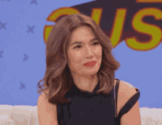 a woman in a black dress is sitting on a couch with the word us behind her