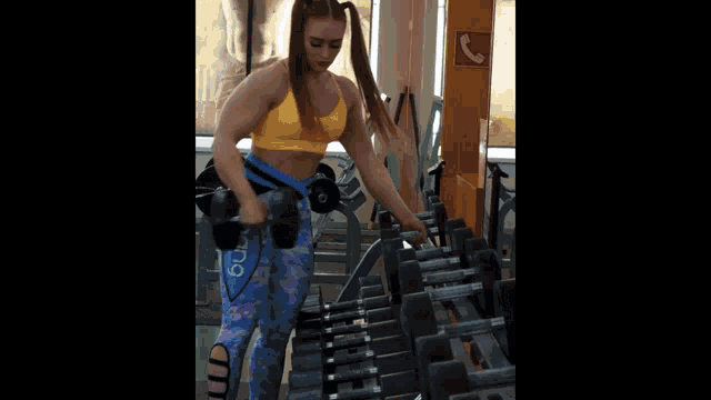 a woman in a yellow top and blue pants is lifting a barbell in a gym