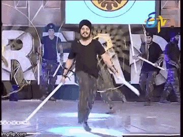 a man in a turban is holding two swords on a stage in front of a tv screen