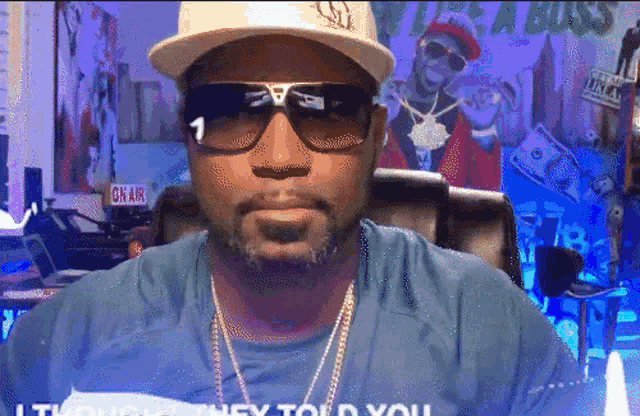 a man wearing sunglasses and a hat is sitting in front of a sign that says " on air "