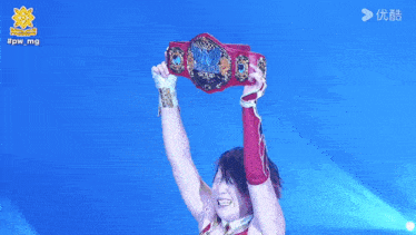 a woman in a wrestling outfit stands in front of a blue background with #pwmg written on it