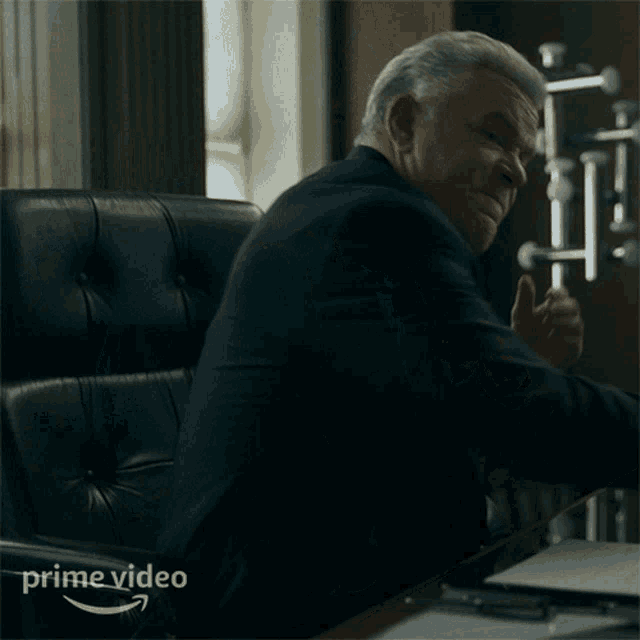 a man in a suit and tie is sitting at a desk with a prime video logo
