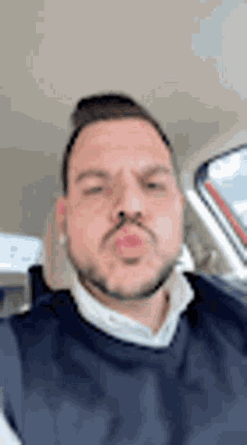 a man with a beard is sitting in a car blowing a kiss .