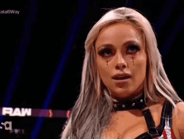 a woman with blonde hair and red eyes is wearing a choker and a black top .