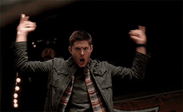 a man wearing a plaid shirt and a grey jacket is holding his arms up in the air