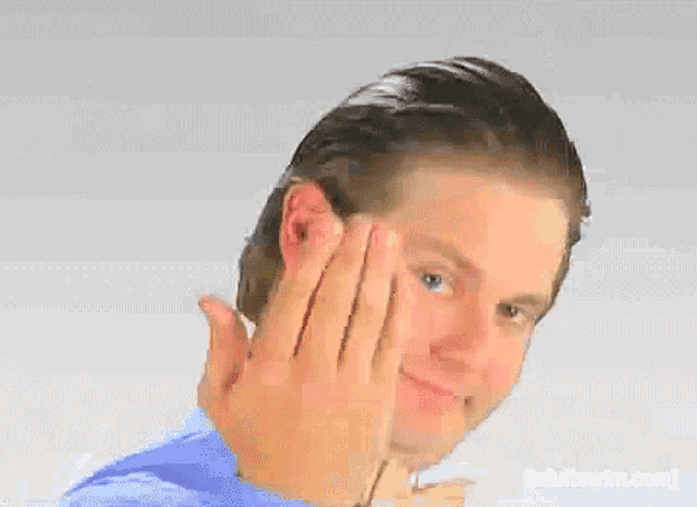 a man in a blue shirt is making a funny face with his hands on his face .