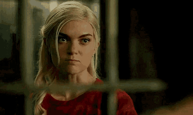a woman in a red dress is behind bars in a prison cell .