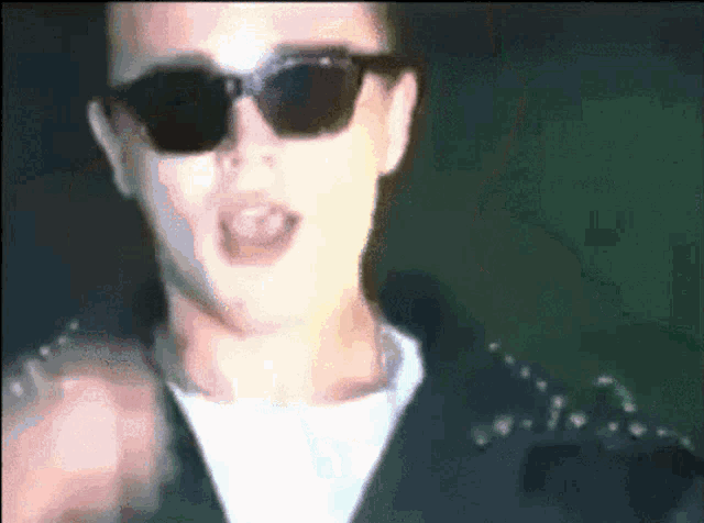 a man wearing sunglasses and a black jacket with studs on the sleeves