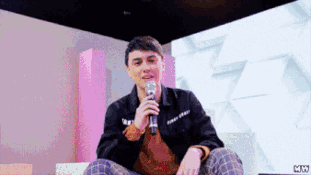 a man in a black jacket is holding a microphone in front of a screen that says mix