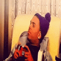a man wearing a purple hat is sitting in a chair holding a red object in his hands .