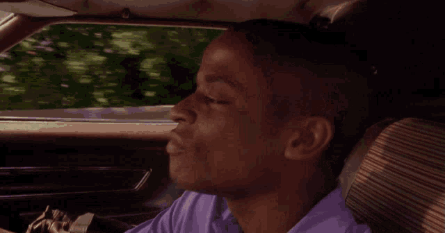 a man in a purple shirt driving a car