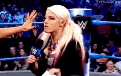 a woman is standing in a wrestling ring holding a microphone and talking to another woman .