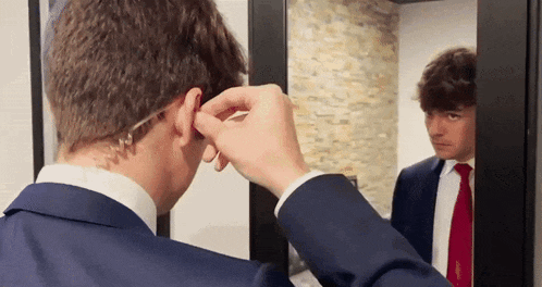 a man in a suit and tie is looking at himself in a mirror