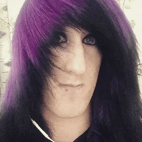 a young man with long black and purple hair is making a funny face .