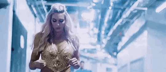 a woman in a gold top is walking down a hallway in a dimly lit room .