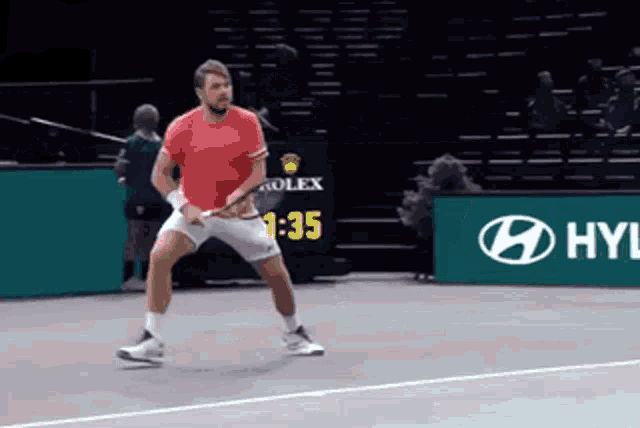 a man in a red shirt is playing tennis on a court sponsored by rolex