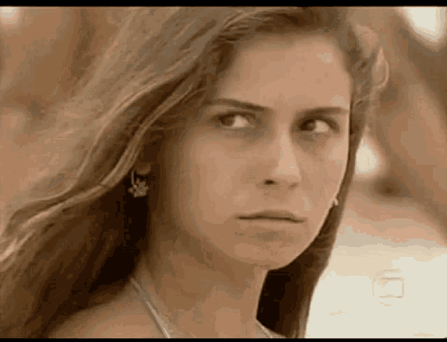 a woman in a bikini and earrings is looking at the camera with a serious look on her face .