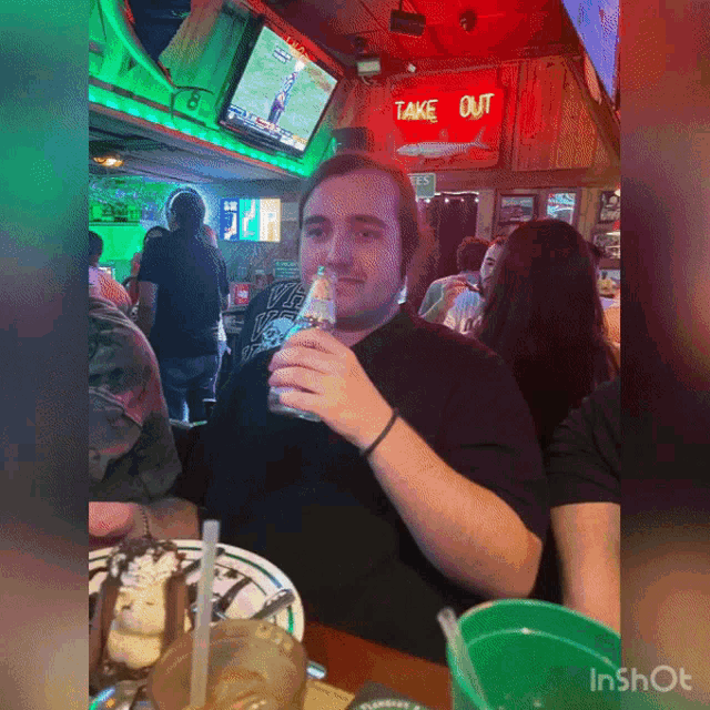 a man sitting at a table in front of a sign that says take out