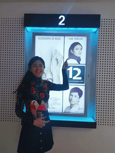 a woman holds a popcorn box in front of a sign that says 12