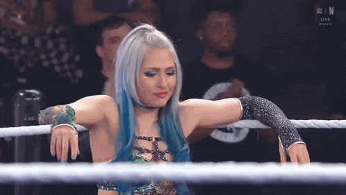 a woman with blue hair is standing in a wrestling ring with the letters n on the bottom