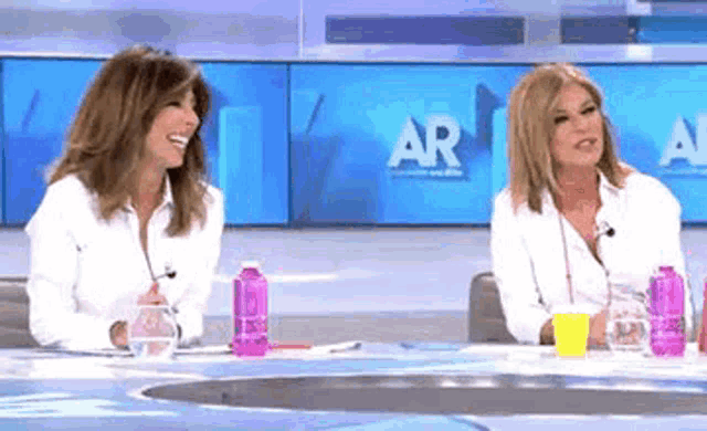 two women are sitting at a table in front of a screen that says ar on it .