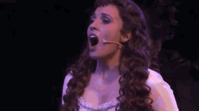 a woman is singing into a microphone on stage while a man looks on .
