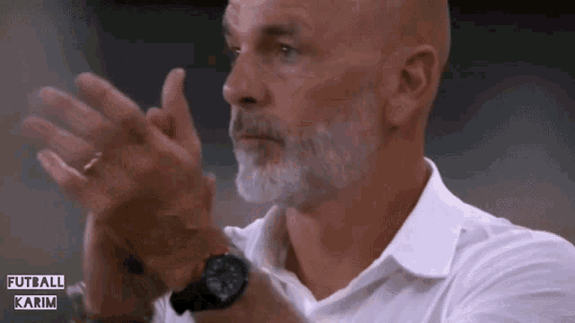 a man with a beard wearing a watch is clapping his hands in front of a sign that says futbol karim