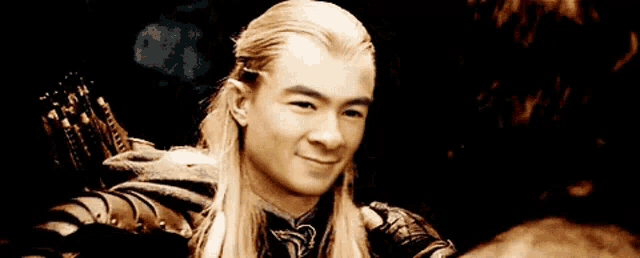 a man with long blonde hair is pointing at the camera with his finger .