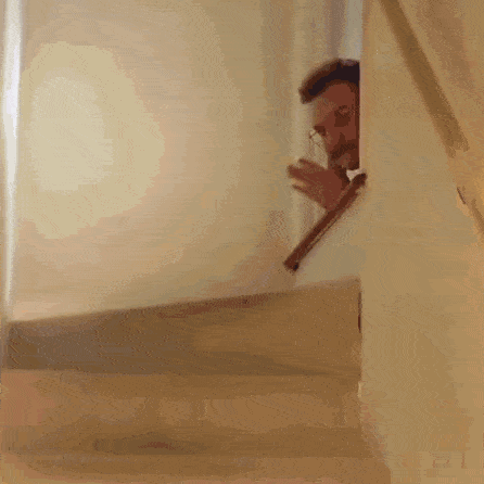 a man in a suit and tie is peeking out from behind a railing on a set of stairs .