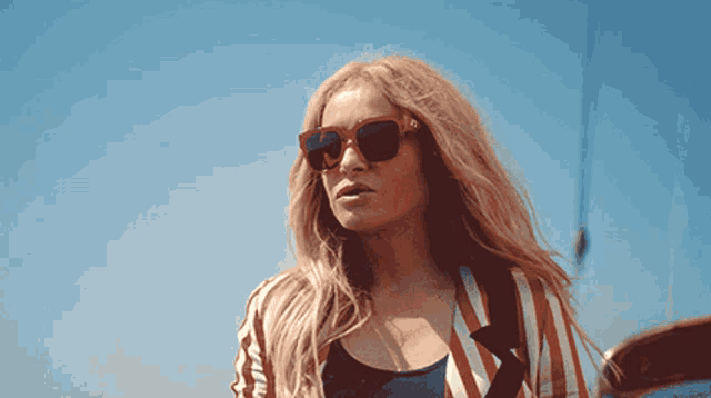 a woman wearing sunglasses and a striped shirt stands in front of a blue sky
