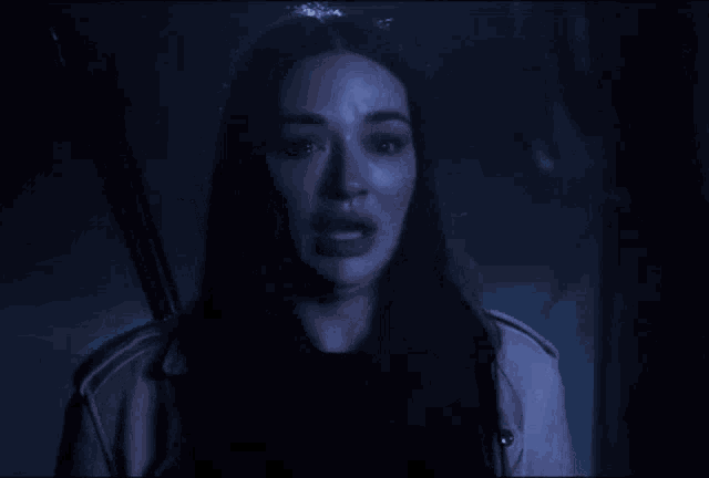 a woman is crying in a dark room with a reflection of herself in the mirror .