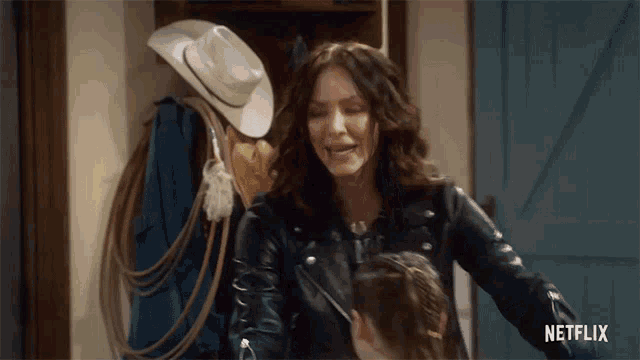 a woman wearing a leather jacket and a cowboy hat is standing next to a little girl .