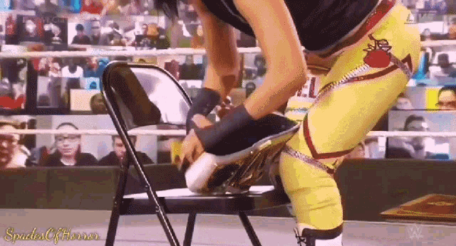 a wrestler is putting his shoes on a chair while a crowd watches .