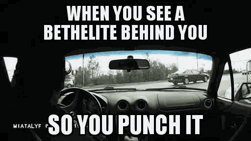 a man is driving a car down a road and a funny meme is written on the dashboard .