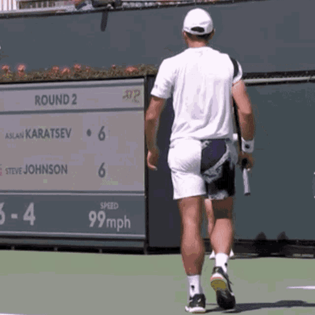 a man walking on a tennis court in front of a scoreboard that says round 2 on it