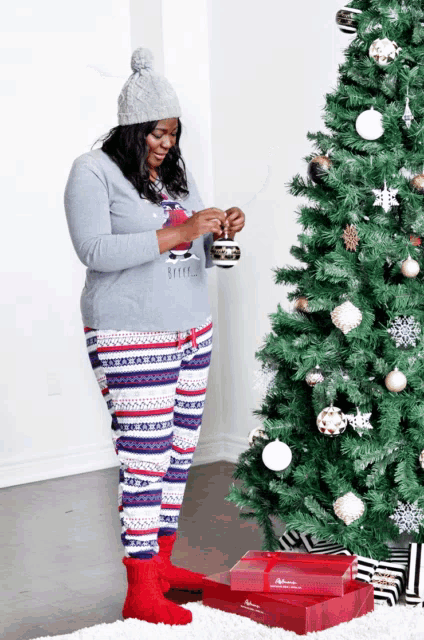 a woman standing in front of a christmas tree holding a bauble