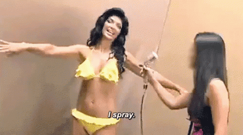 a woman in a bikini is spraying another woman 's arm with a spray gun .