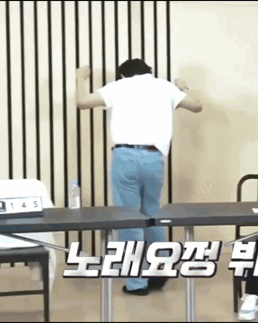 a man in a white shirt and blue jeans is standing in front of a table with korean writing on it .